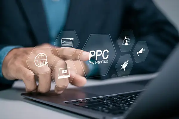 Hand clicking on PPC button over laptop surrounded by icons
